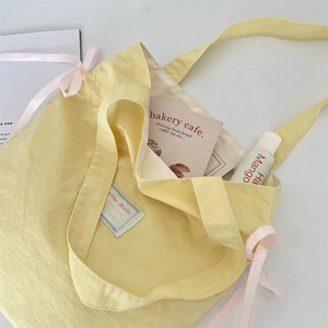 Detail of light yellow canvas tote bag with pink ribbon bow and akka Studio label