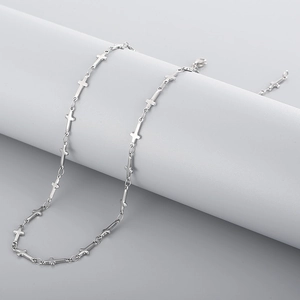 Détail d'un collier chaîne à croix en acier inoxydable argenté posé sur un support blanc