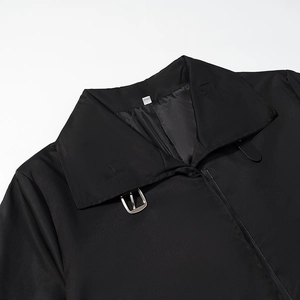 Detail of the high collar with metallic buckle on a long black minimalist trench coat