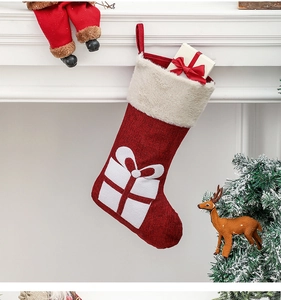 Red knit Christmas stocking with gift box embroidery hanging on a white fireplace mantel