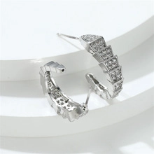 Detailed macro view of silver snake scale C-hoop earrings with pave-set zircon stones