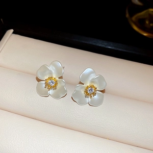Detailed close-up of pearl white flower earrings with gold center and zircon in a leather box