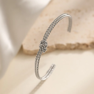Silver twisted rope open bangle with a central knot detail on elegant stone background