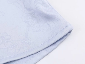 Nahaufnahme der hellblauen Jacquard-Stoffstruktur und der sauberen Saumnaht am Damenhemd