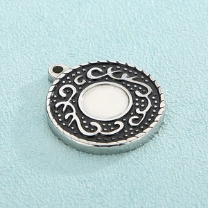 Macro shot of silver titanium steel circular pendant with black enamel scroll patterns