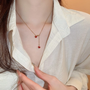 Golden necklace detail with two red oil-dripped heart pendants on a model
