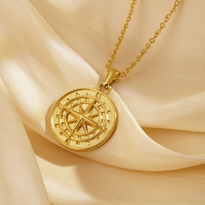 Golden stainless steel compass pendant necklace displayed on elegant champagne silk fabric