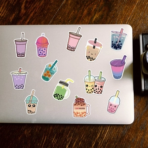 Various cute bubble tea stickers arranged on a silver laptop and dark wood table