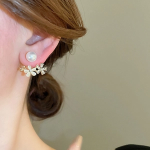 Close-up of pearl flower earrings with cat eye stones worn by a model in warm light