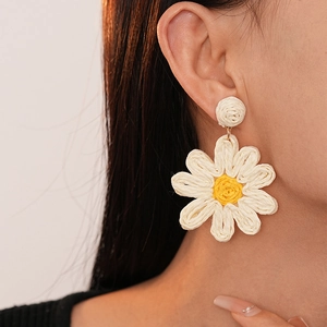 Close-up of model wearing a handmade woven white daisy flower earring with yellow center