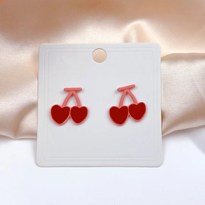 Detail view of pink cherry heart earrings on a satin background with a soft gloss
