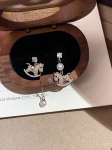 Detail of asymmetric gold rocking horse earrings with pearls and crystals in a jewelry box
