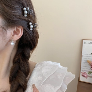 Close-up of elegant pearl hair clips and Saturn-shaped pearl earrings on a model