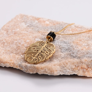 Golden hollow monstera leaf pendant necklace on a natural pink stone background