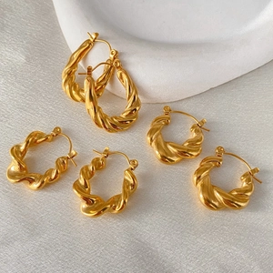 Close-up of twisted gold hoop earrings in two sizes on white textured background