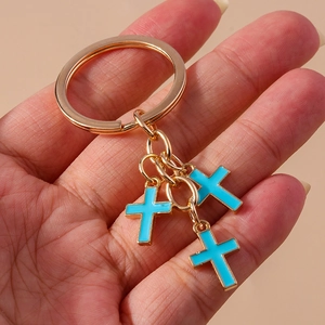 Close-up of hand holding golden keychain with three sky blue enamel cross pendants