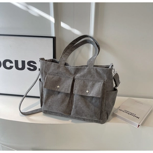 Detail of grey corduroy tote bag showing front pockets with metal snap buttons