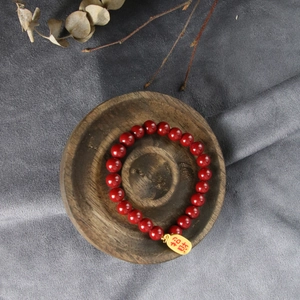 Deep red beaded bracelet with golden lucky charm on wooden display tray with zen styling