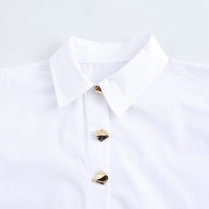 Detail of white shirt collar featuring textured fabric and unique gold irregular metal buttons