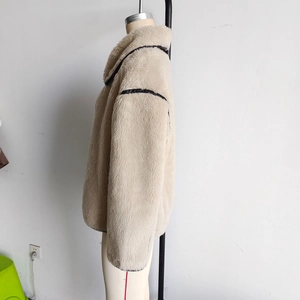 Detail of beige faux fur jacket with stylish black leather trim on collar and sleeves