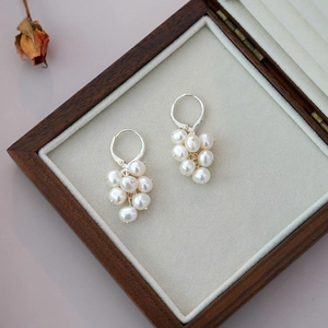 Detail view of cluster pearl drop earrings with silver finish on a wooden jewelry box