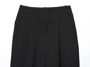 Detail view of high-waist black trousers with belt loops and elegant pleated front texture