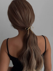 Detailed back view of a model wearing a golden metallic bow hair tie on a ponytail