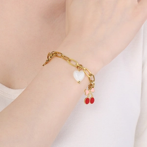 Détail du bracelet chaîne dorée avec breloque cœur blanc et pendentif cerise sur poignet