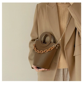 Detail view of brown bucket bag with circular handle and decorative thick chain strap