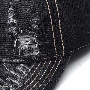 Detailed close-up of distressed black denim baseball cap with frayed holes and thick stitching
