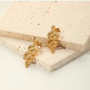 Dettaglio degli orecchini a forma di serpente in oro 18K su sfondo di pietra beige
