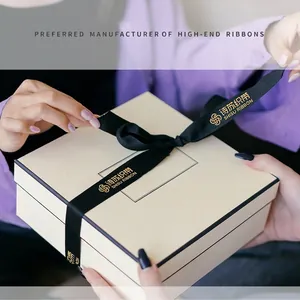 Black satin ribbon with gold logo tied on a cream gift box for birthdays and events