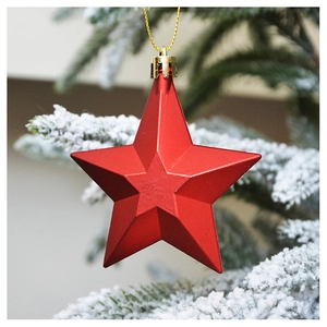 Close-up of matte red star ornament hanging on a snowy Christmas tree branch
