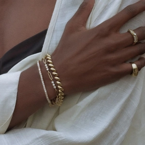 Close-up of gold-plated tennis bracelets and rings with white stones on a model