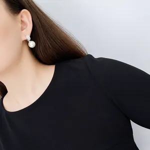 Detalle de un elegante pendiente de perla blanca redonda con circonitas en una modelo