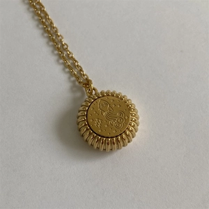 Close-up of golden Aquarius zodiac pendant with engraved symbol and textured edge detail