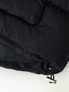 Detailed macro of black puffer jacket hem featuring metallic silver toggle and elastic drawstring