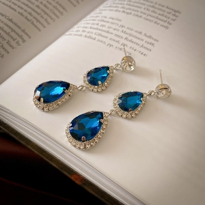 Close-up of elegant blue teardrop crystal earrings with silver diamond setting on a book