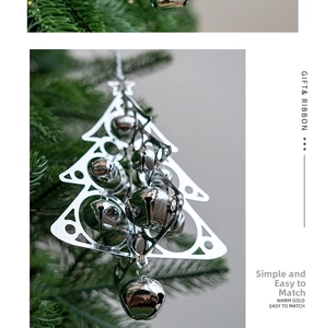 Silver metal Christmas tree ornament with bells hanging on a lush green pine branch