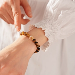 Detailed view of Tiger Eye bead bracelet with gold foil charm on a person's wrist