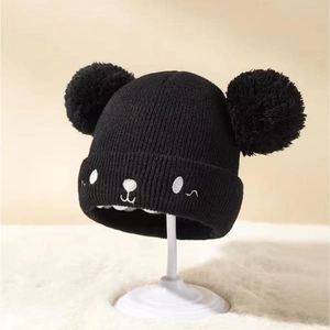 Detail der schwarzen Kinderstrickmütze mit flauschigen Bommeln und Bärenstickerei