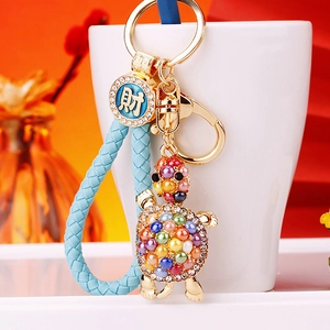 Detail of turtle keychain with blue braided strap, rhinestones and golden medal charm