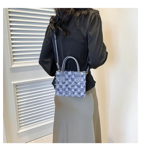 Detail of blue checkerboard denim handbag with frayed edges and long shoulder strap