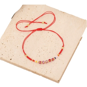 Handmade red rope bracelet with purple crystal beads and gold accents on stone base