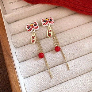 Detail view of lion dance earrings with red beads and long gold chain tassels
