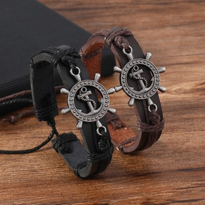 Close-up of black and brown braided leather bracelets with metallic anchor and helm charms
