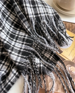 Close-up of black and white checkered scarf with fringe on a cozy wooden desk setup