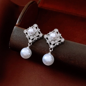 Macro shot of silver pearl earrings with hollow diamond shape and zircon accents