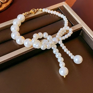 Dettaglio bracciale di perle con fiocco dorato su un vassoio di pelle per gioielli