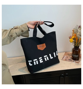 Detail of black canvas tote bag with white lettering and a brown leather logo patch